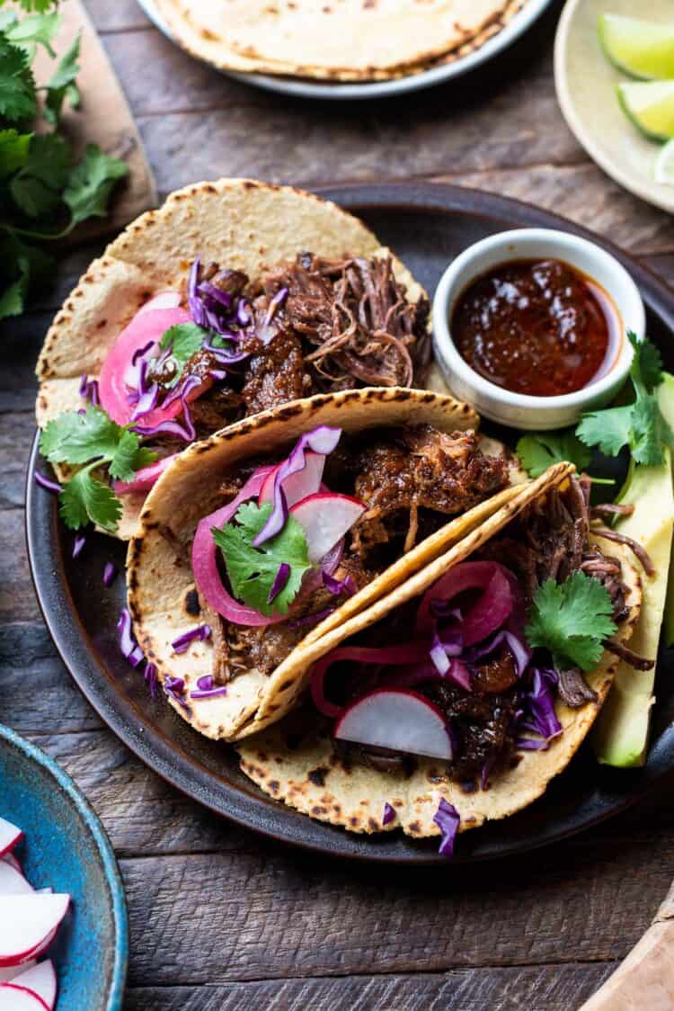 Short rib tacos on a plate with chipotle sauce on the side.