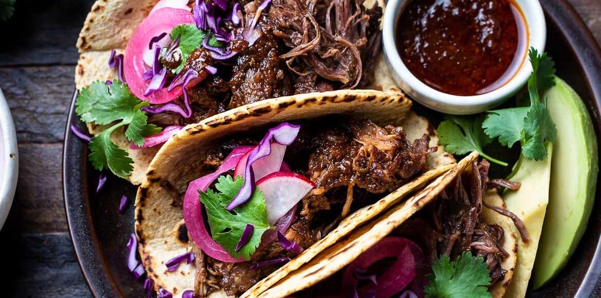 Short Rib Tacos on a plate garnished with red cabbage, pickled onions, radish, and cilantro.