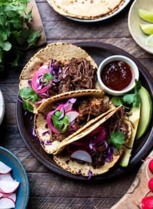 Short Rib Tacos on a plate garnished with red cabbage, pickled onions, radish, and cilantro.