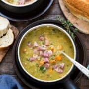 A serving of slow cooker split pea soup dished up in a bowl and topped with seasonings and small squares of ham.