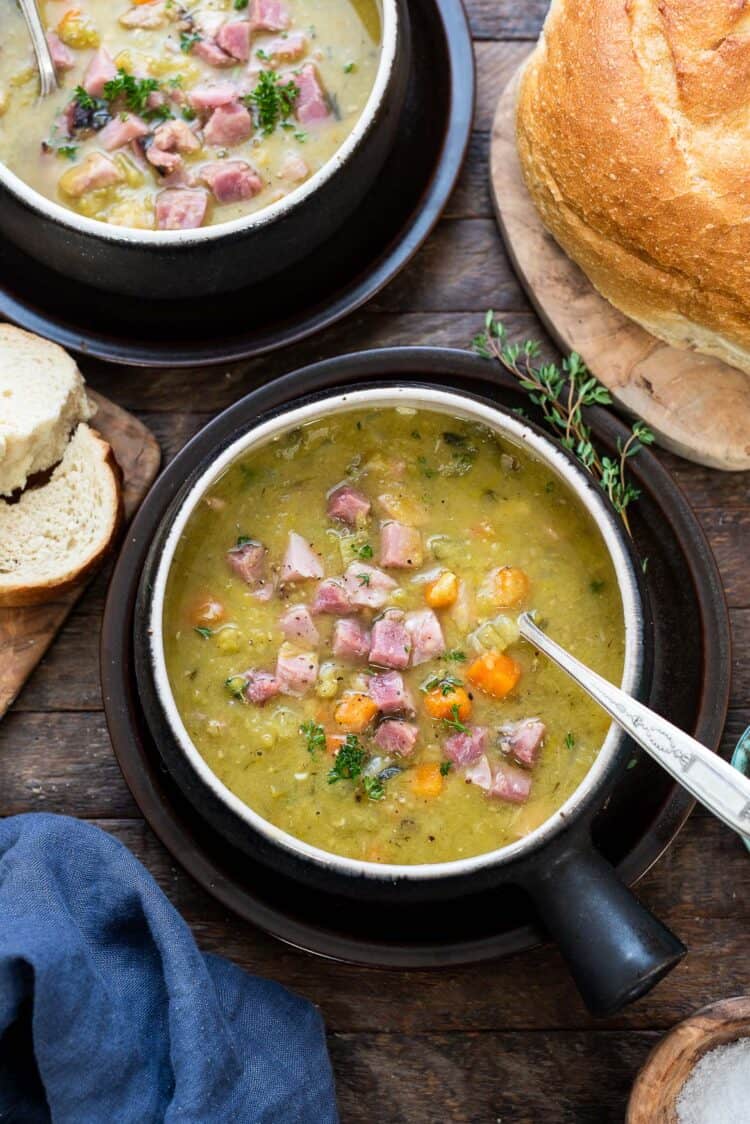 A serving of slow cooker split pea soup dished up in a bowl and topped with seasonings and small squares of ham.