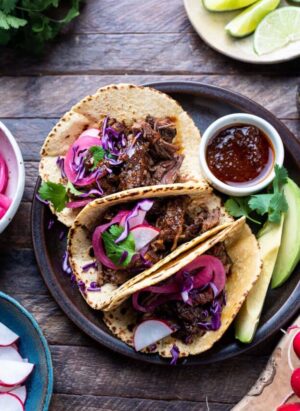 Short rib tacos on a plate with chipotle sauce on the side.