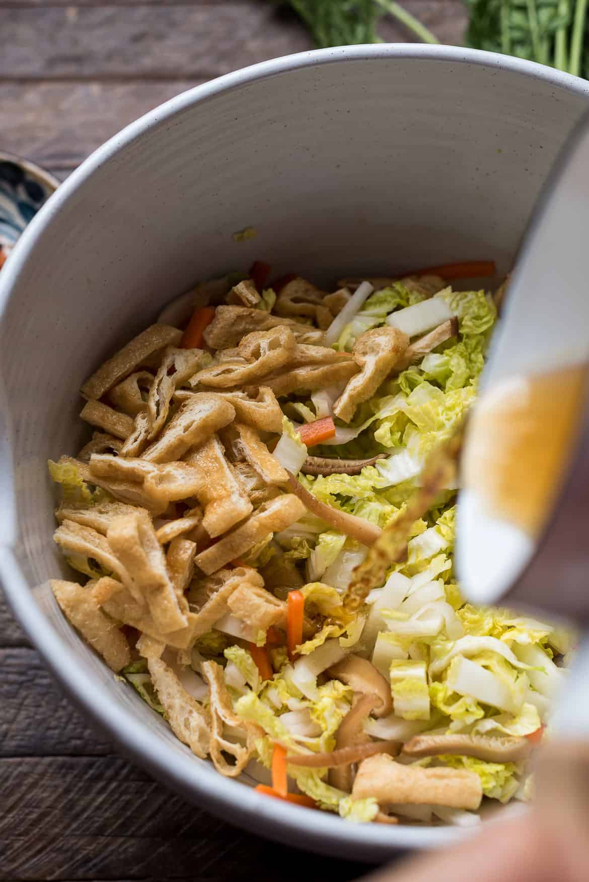 Adding vinegar mixture to Napa cabbage in a bowl.