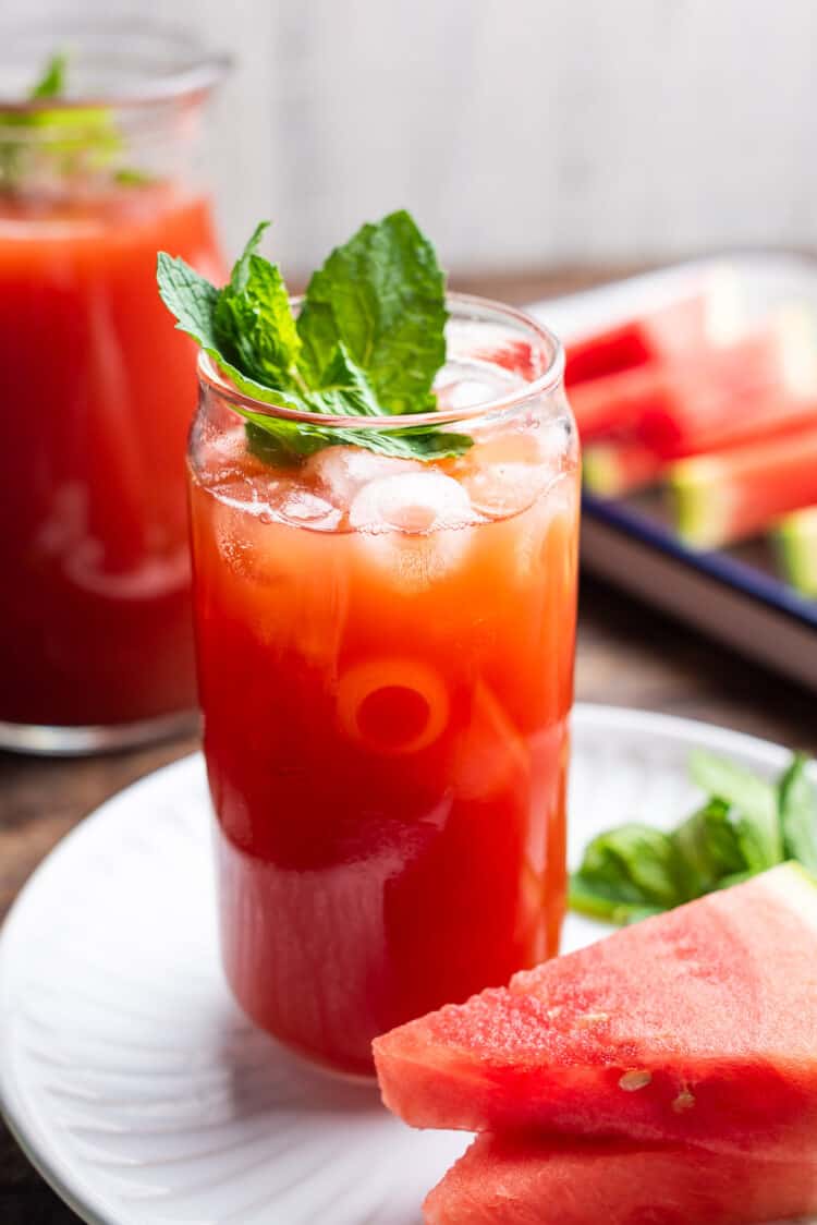 A glass of Watermelon Sweet Tea with a pitcher in the background.