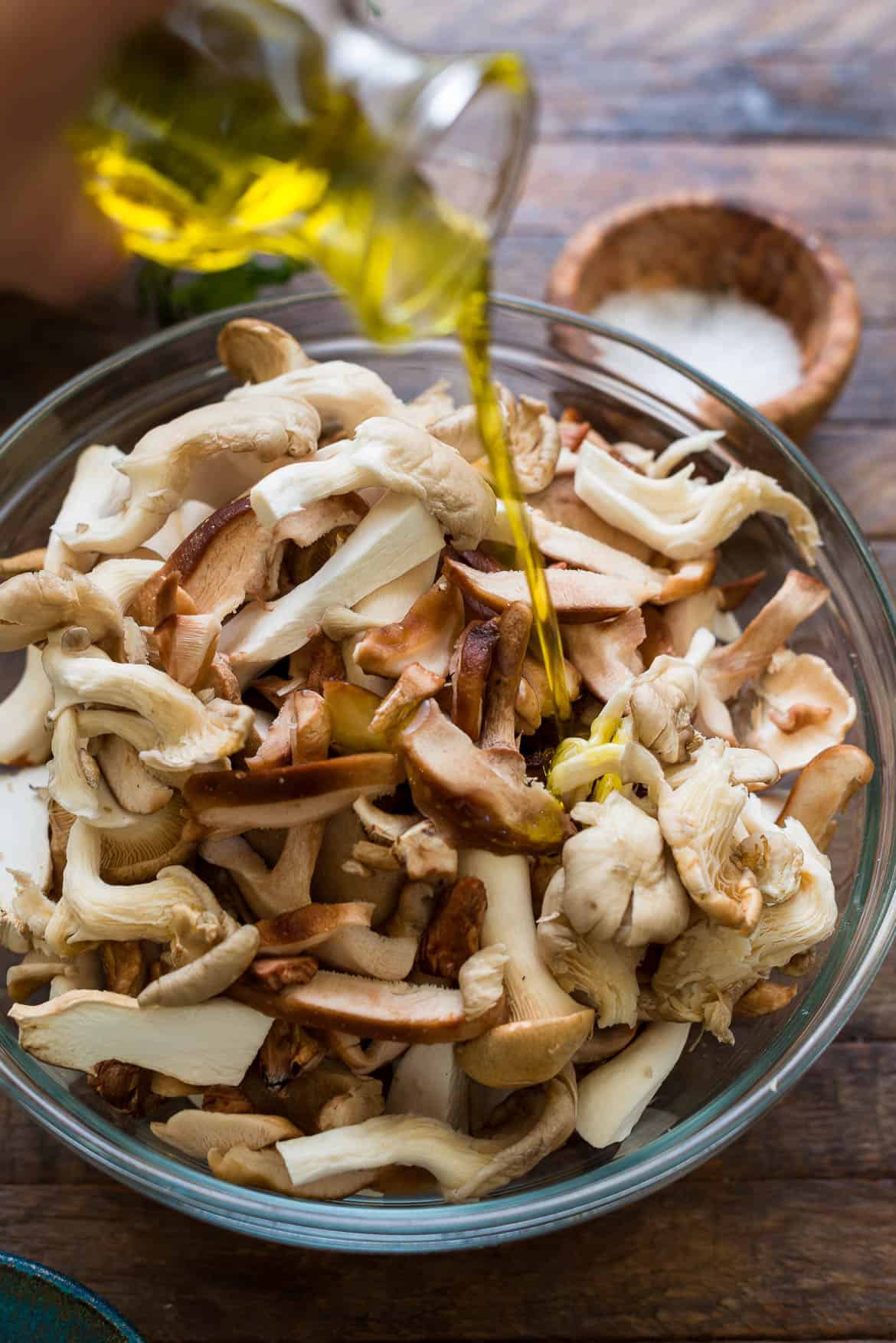 Drizzling olive oil over mushrooms in a glass bowl.