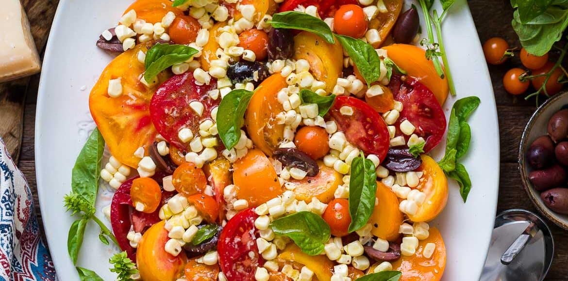 Tomato Salad with Corn and Kalamata Olives on a platter with fresh basil.