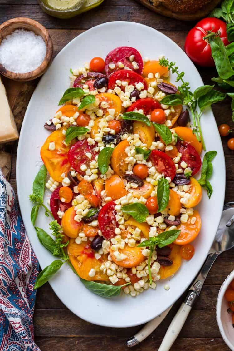 Tomato salad with basil, corn, and olives on a platter.