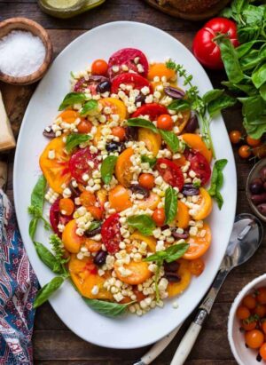 Tomato Salad with Corn and Kalamata Olives on a platter with fresh basil.