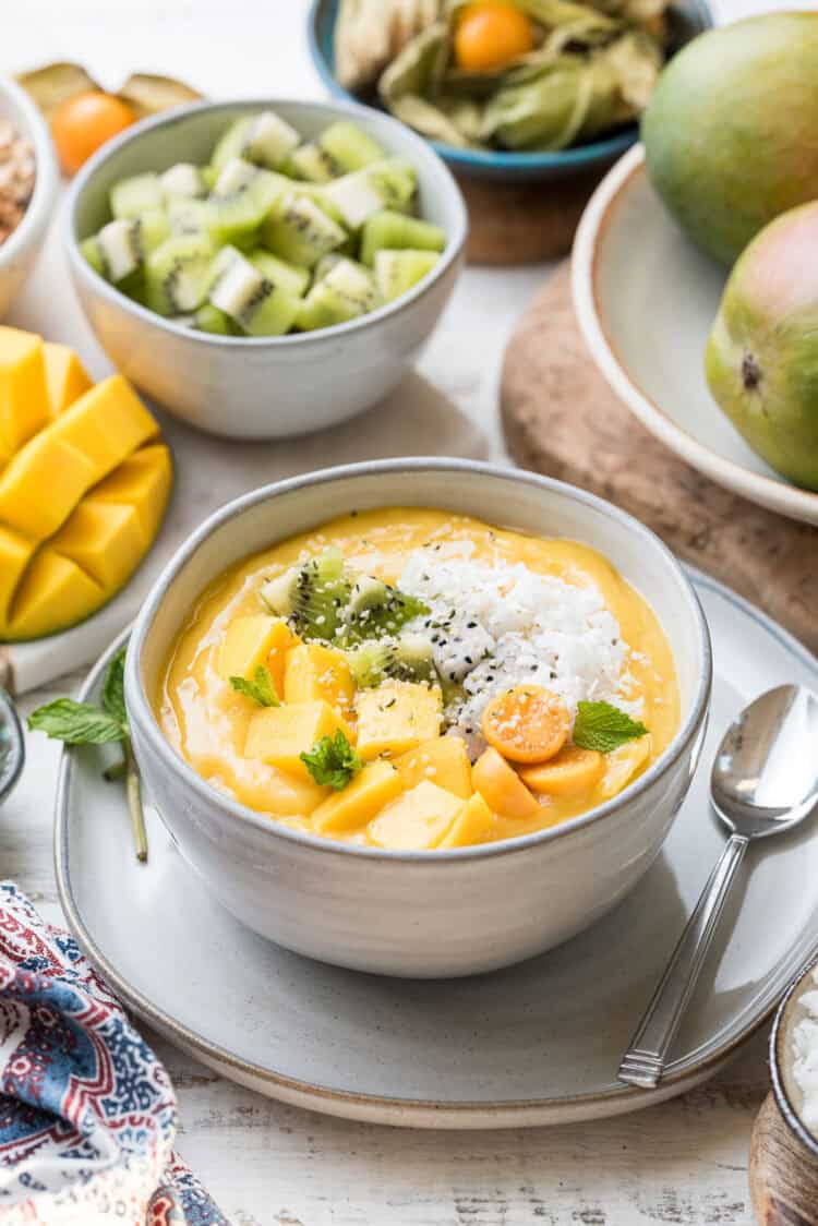 Tropical Smoothie Bowl in a white bowl topped with fresh mango, golden berries, and shredded coconut.