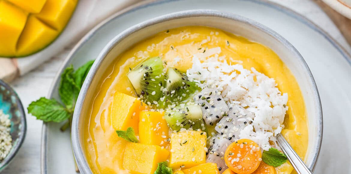 Tropical Mango Smoothie Bowl in a white bowl with mango topped with fresh mango, golden berries, shredded coconut, and hemp seeds.