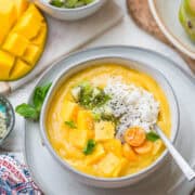 Tropical Mango Smoothie Bowl in a white bowl with mango topped with fresh mango, golden berries, shredded coconut, and hemp seeds.