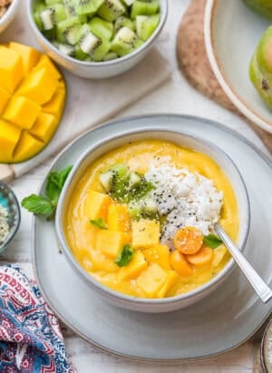 Tropical Mango Smoothie Bowl in a white bowl with mango topped with fresh mango, golden berries, shredded coconut, and hemp seeds.