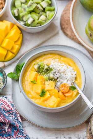 Tropical Mango Smoothie Bowl in a white bowl with mango topped with fresh mango, golden berries, shredded coconut, and hemp seeds.