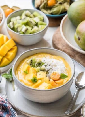Tropical Smoothie Bowl in a white bowl topped with fresh mango, golden berries, and shredded coconut.