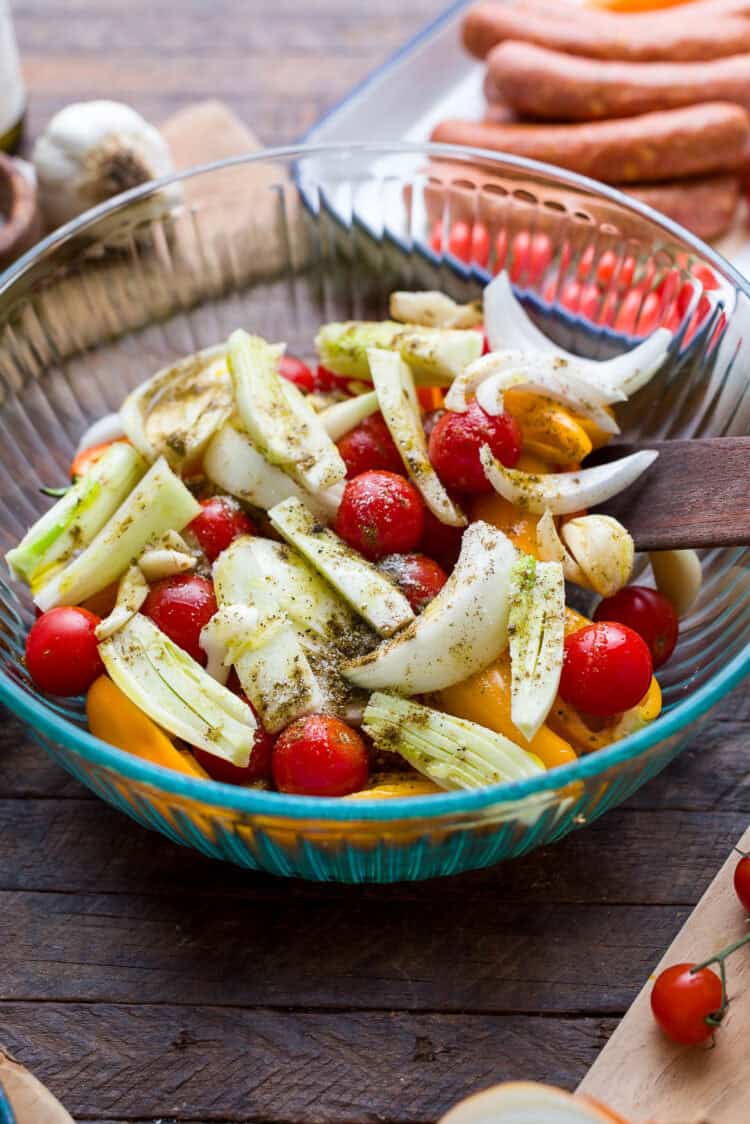 Seasoned peppers, onions, fennel, garlic, and tomatoes in a glass bowl.