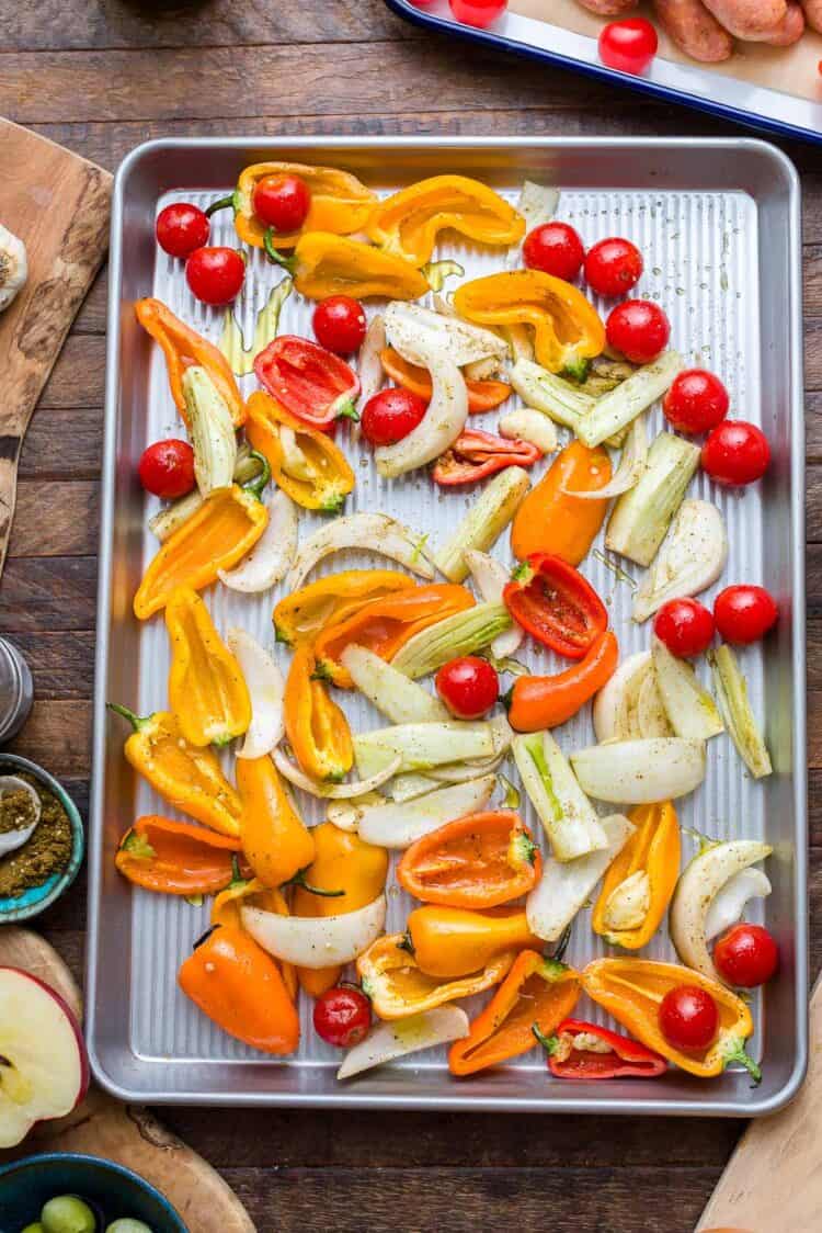 Seasoned peppers, onions, fennel, tomatoes on a sheet pan.