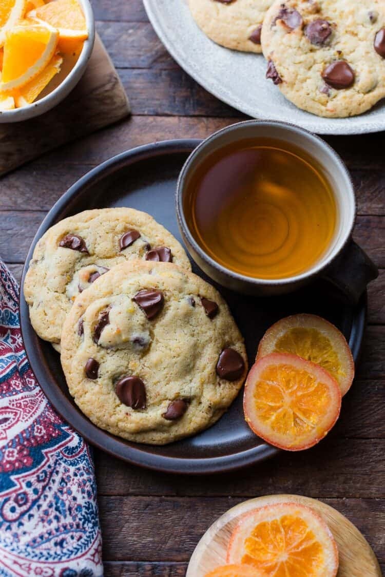 Large, bakery-style Dark Chocolate Orange Cookies on a plate, served with a cup of tea.