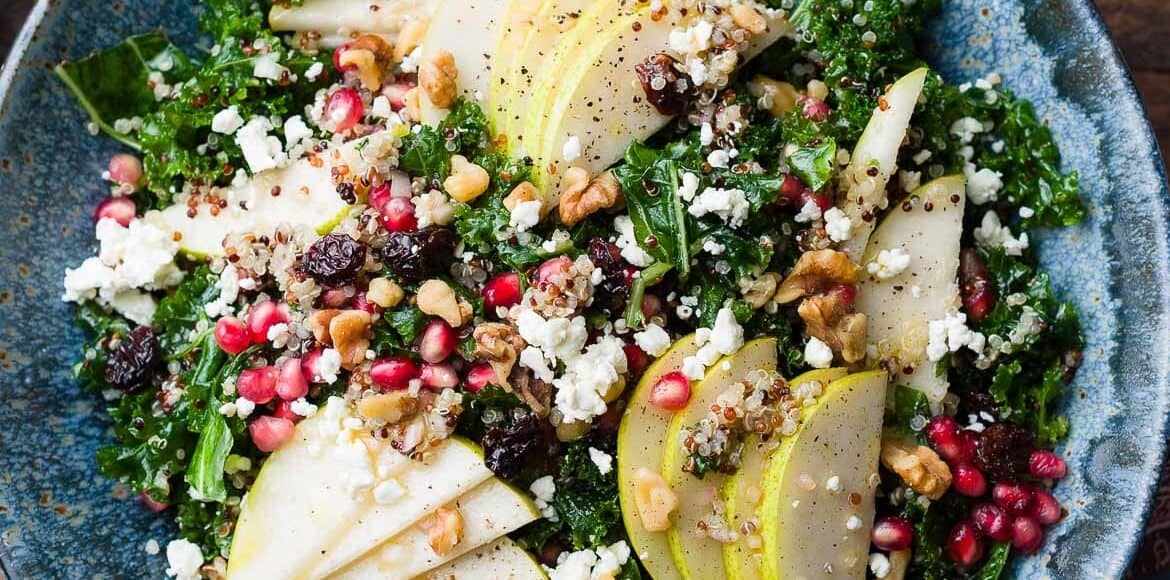 Kale and Quinoa Fall Salad with pears, pomegranates, feta, walnuts, dried cherries or cranberries, in a blue bowl.