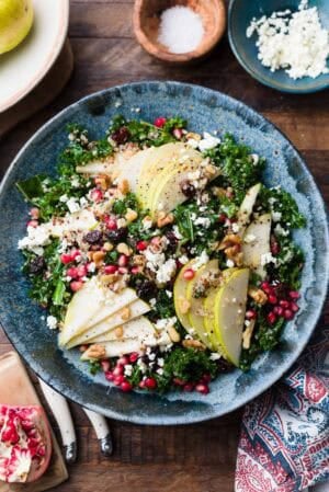 Kale and Quinoa Fall Salad with pears, pomegranates, feta, walnuts, dried cherries or cranberries, in a blue bowl.