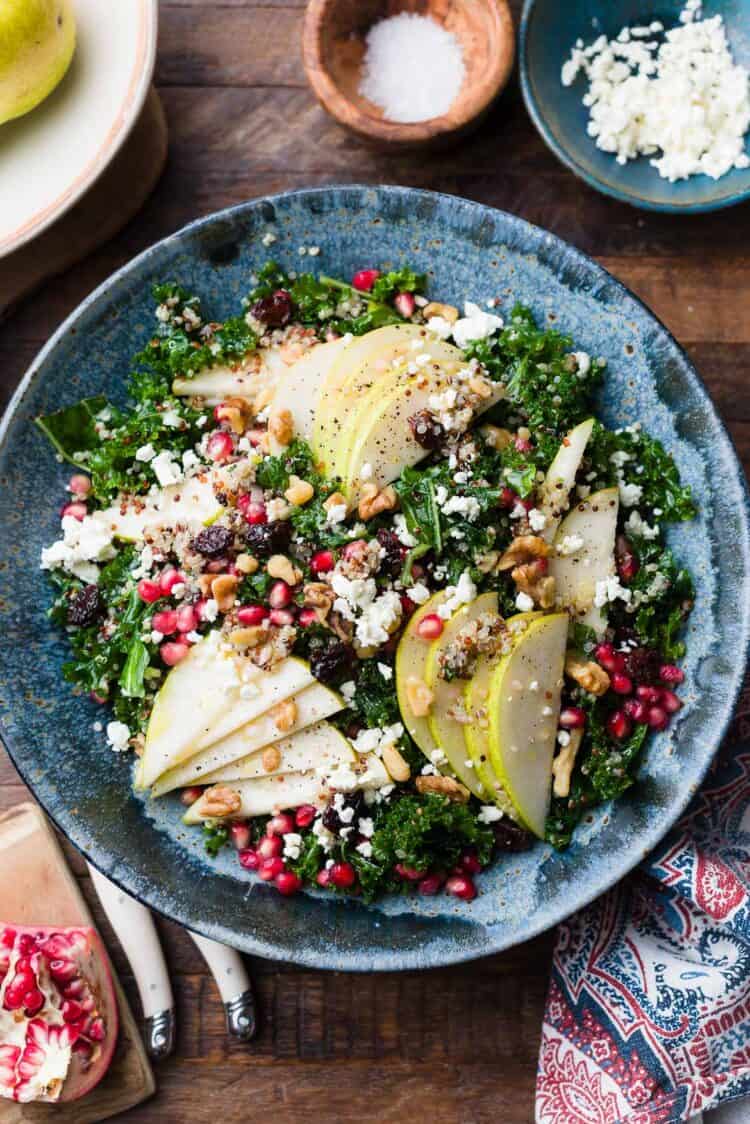 Kale and Quinoa Fall Salad with pears, pomegranates, feta, walnuts, dried cherries or cranberries, in a blue bowl.