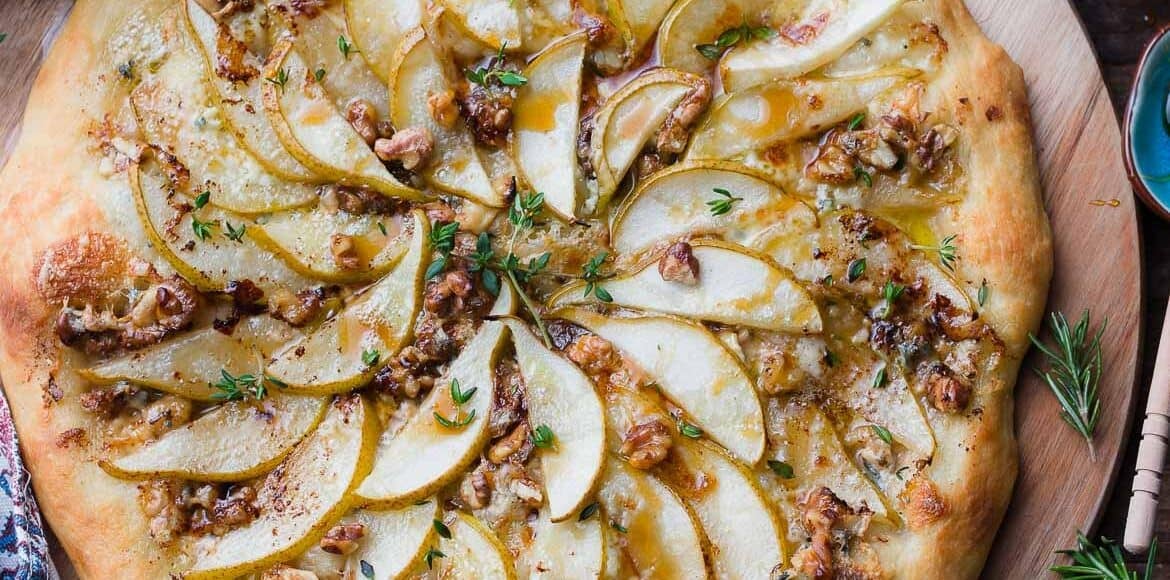 Pear, Walnut, and Gorgonzola Pizza drizzled with honey on a wooden board.