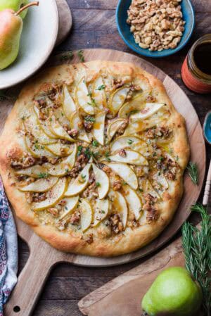 Pear, Walnut, and Gorgonzola Pizza drizzled with honey on a wooden board.