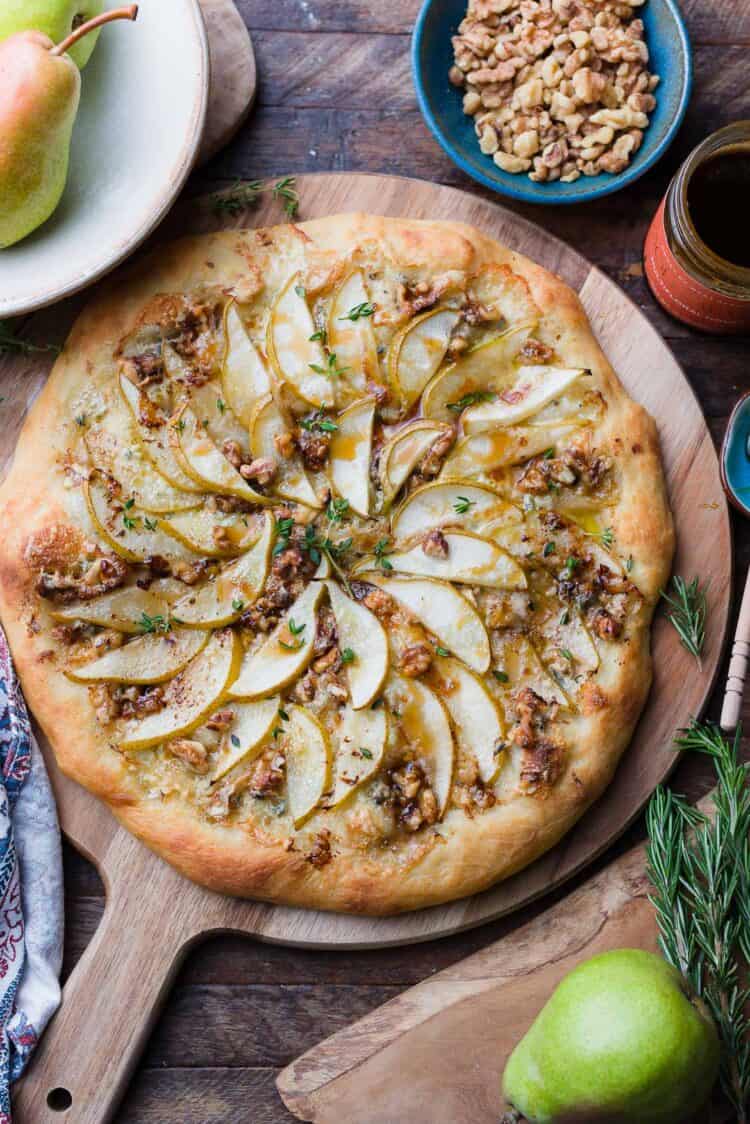 Pear, Walnut, and Gorgonzola Pizza drizzled with honey on a wooden board.