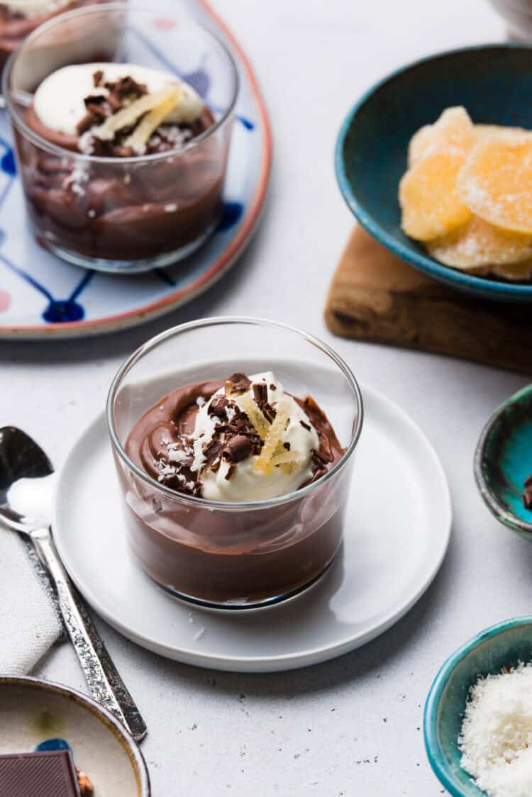 Coconut Chocolate Pudding in a serving glass, garnished with chocolate curls, crystalized ginger, and shredded coconut.