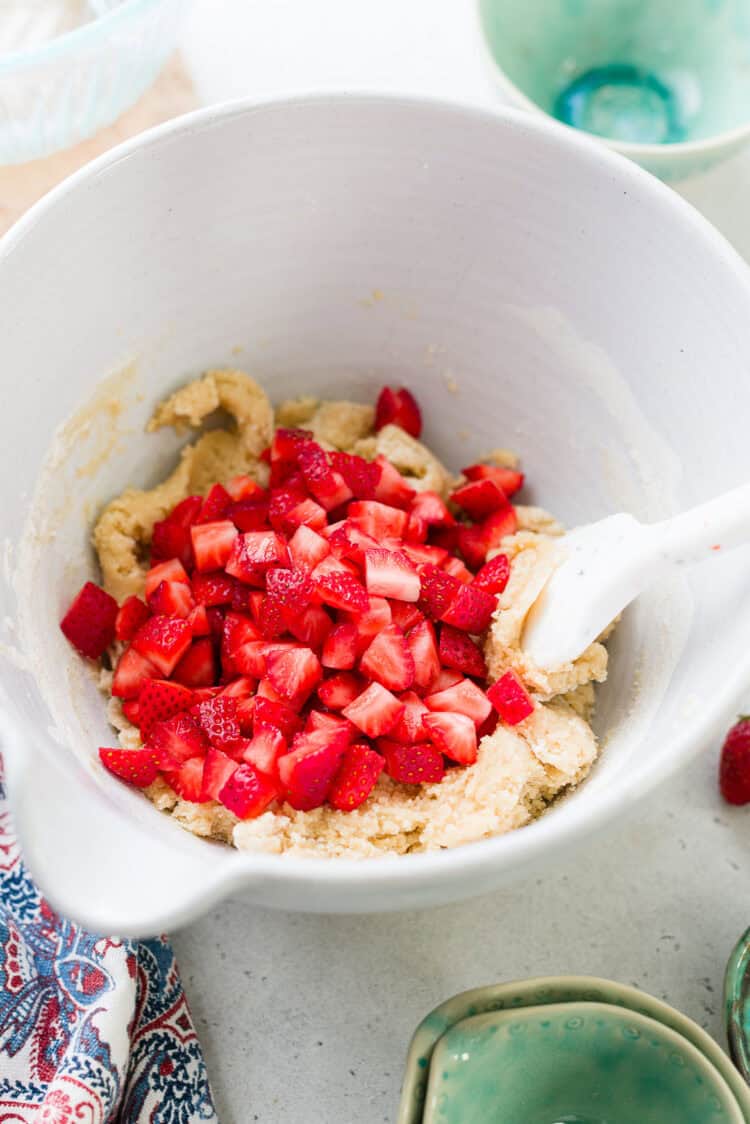 Adding strawberries to cookie batter in a bowl.