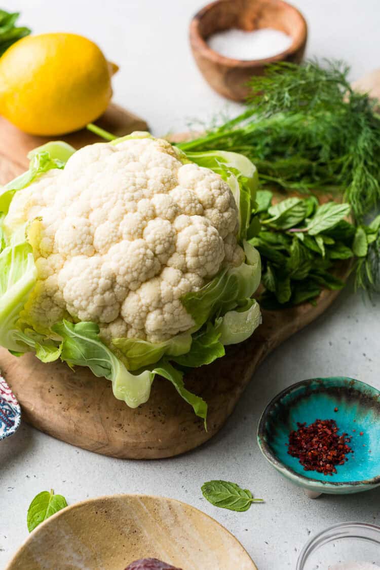 A whole cauliflower and ingredients for Tahini-Charred Cauliflower with Dates and Mint.