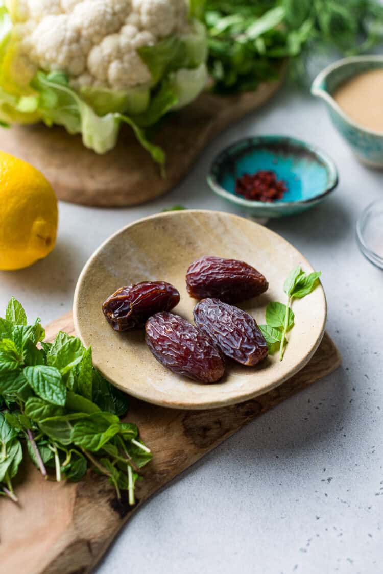 Dried dates in a dish, and ingredients for Tahini-Charred Cauliflower with Dates and Mint.