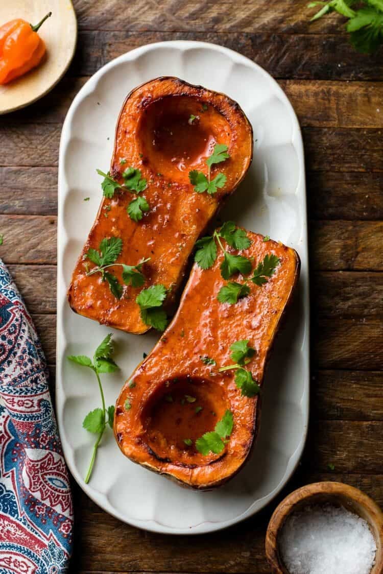Roasted butternut squash halves on a platter, garnished with cilantro.