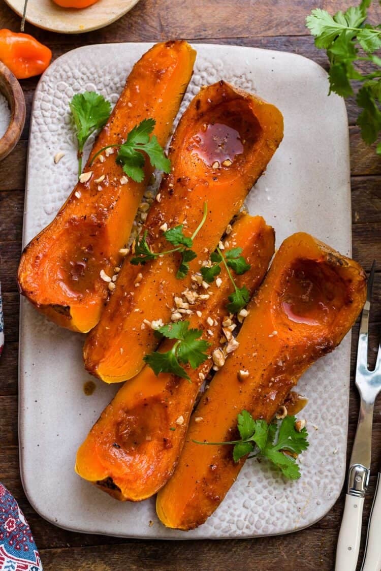 Slices of roasted butternut squash on a platter, garnished with cilantro and crushed hazelnuts.