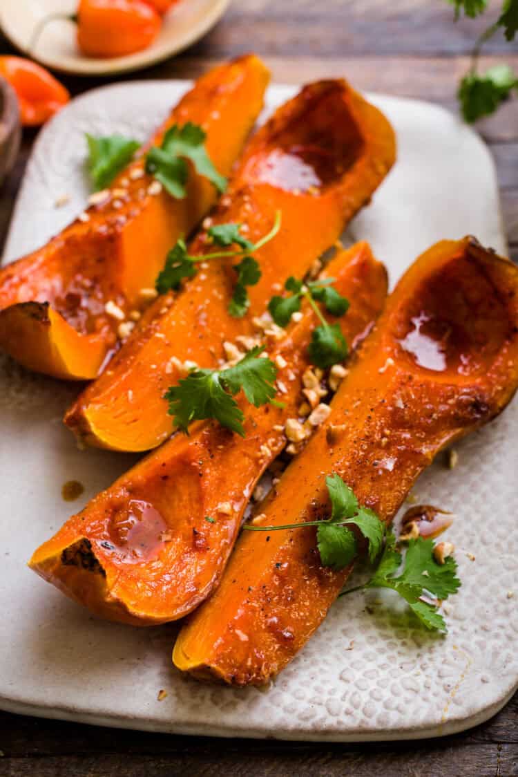 Slices of roasted butternut squash on a platter, garnished with cilantro and crushed hazelnuts.