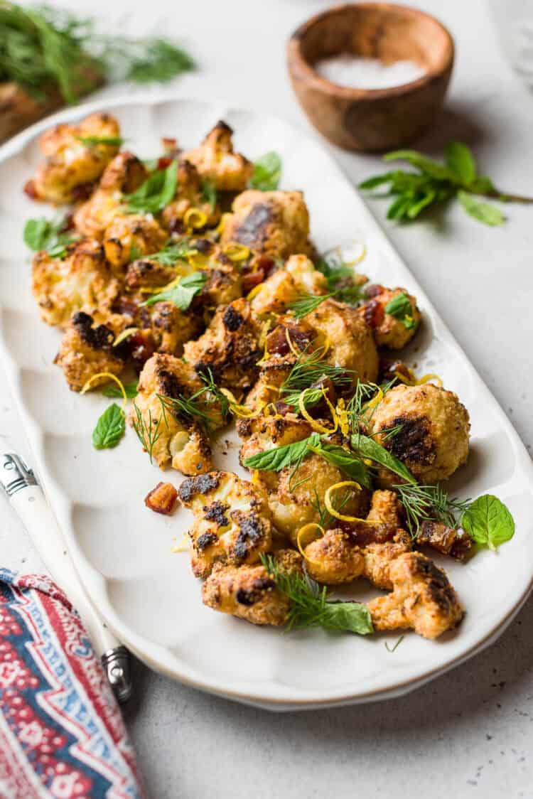 Tahini-Charred Cauliflower garnished with dates, mint, dill, and lemon zest, on a serving platter.