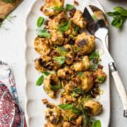 Tahini-Charred Cauliflower garnished with dates, mint, dill, and lemon zest, on a serving platter.