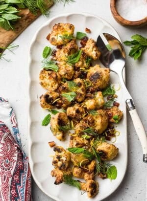 Tahini-Charred Cauliflower garnished with dates, mint, dill, and lemon zest, on a serving platter.