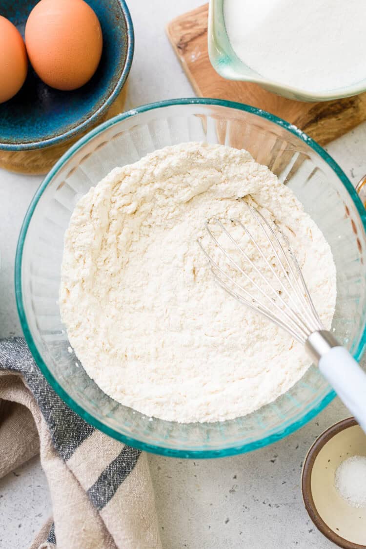 Flour in a bowl with a whisk for ube crinkle cookies.