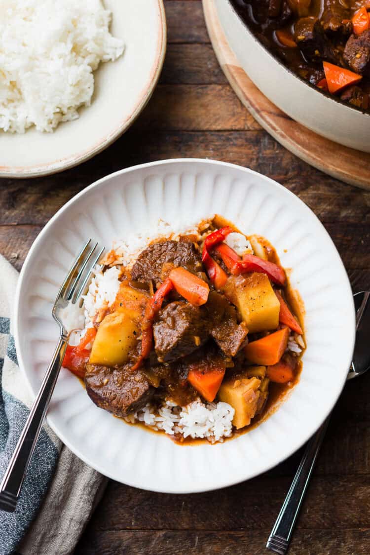 Mechado (Filipino Beef Stew) served over a bed of white rice in a white bowl.