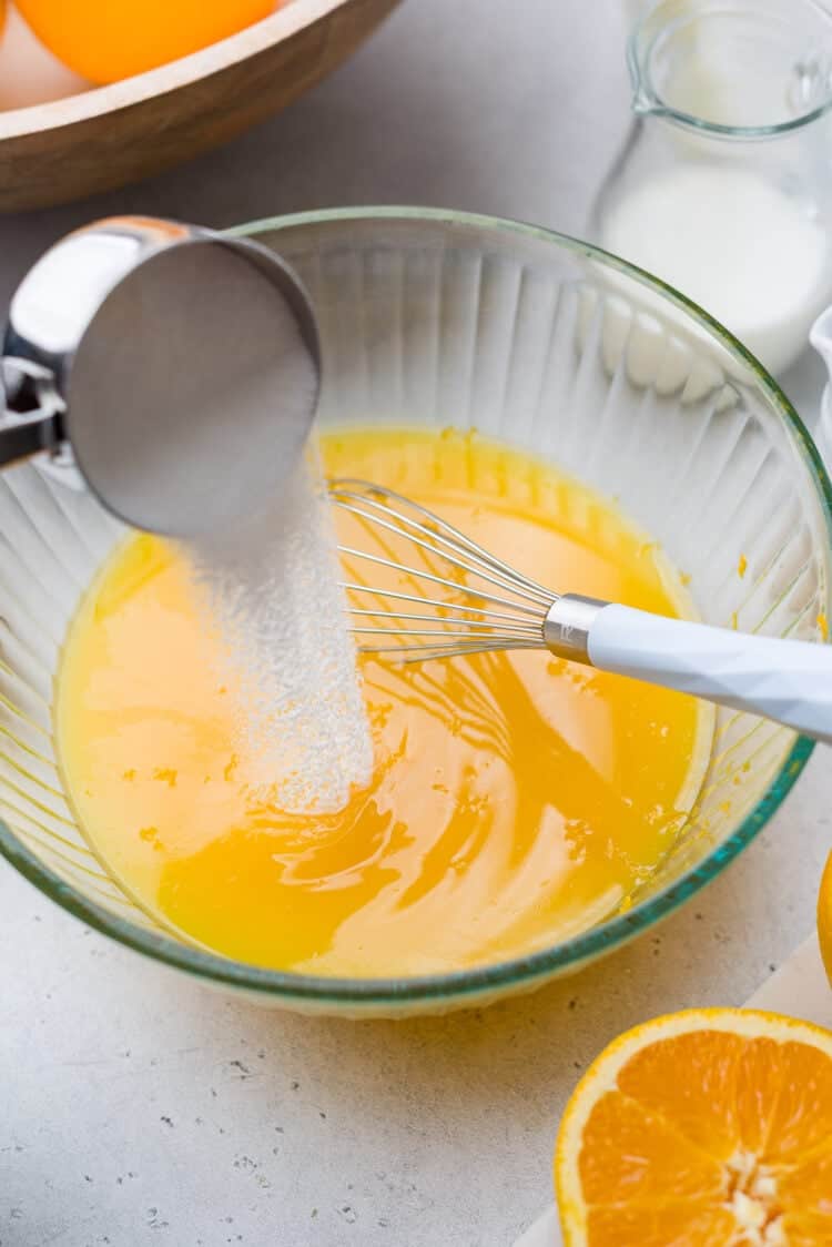 Adding sugar to orange juice for an orange sherbet recipe.