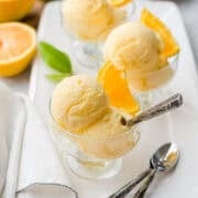 Scoops of orange sherbet in glass dessert dishes, garnished with slices of fresh orange.