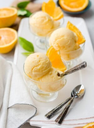 Scoops of orange sherbet in glass dessert dishes, garnished with slices of fresh orange.
