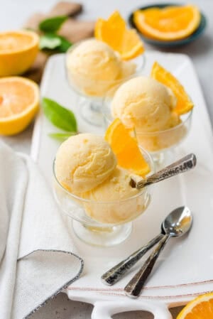 Scoops of orange sherbet in glass dessert dishes, garnished with slices of fresh orange.