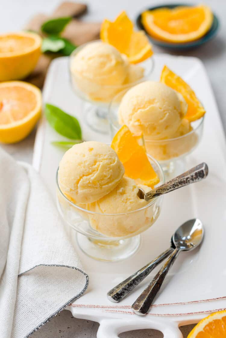 Scoops of orange sherbet in glass dessert dishes, garnished with slices of fresh orange.
